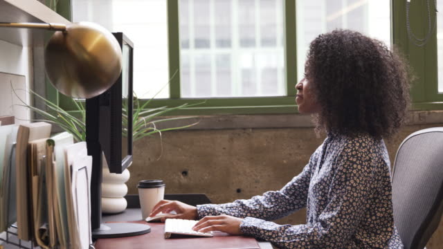 Junge-schwarze-Frau-mit-Computer-in-einem-Büro,-Seitenansicht