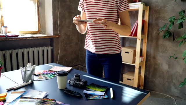 Tilt-Up-Schuss-von-jungen-reiseblogger-Bilder-von-ihrem-Schreibtisch-mit-Smartphone-zu-machen.-Sie-ist-verschiedene-Dinge-auf-ihrem-Tisch-bewegen-und-schießen.