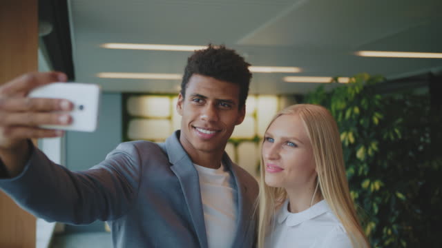 Laughing-diverse-coworkers-taking-selfie-in-office.-Cheerful-black-man-with-laughing-blond-woman-taking-selfie-with-smartphone-in-modern-office-having-fun