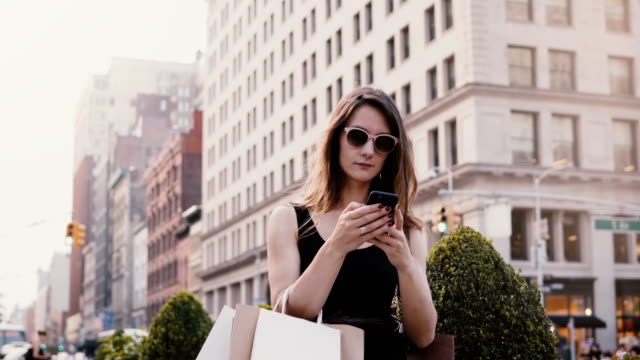 Glücklich-attraktive-kaukasischen-geschäftsfrau-mit-Einkaufstüten-im-Chat-mit-Freunden-auf-Smartphone-social-app-in-New-York