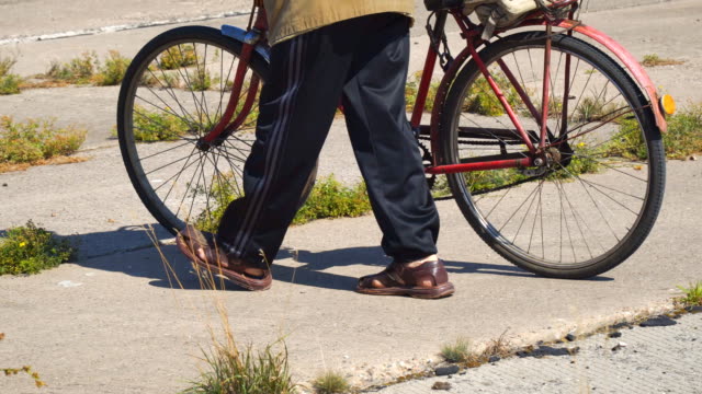 Anciano,-caminando-por-la-calle-con-una-bicicleta-vieja