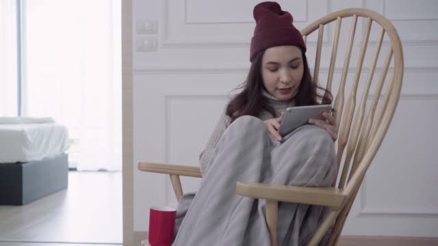 Beautiful-attractive-Asian-woman-using-tablet-for-texting-and-reading-while-sitting-on-chair-when-relax-in-living-room-at-home.-Lifestyle-women-at-home-in-Christmas-and-New-year-holidays-concept.