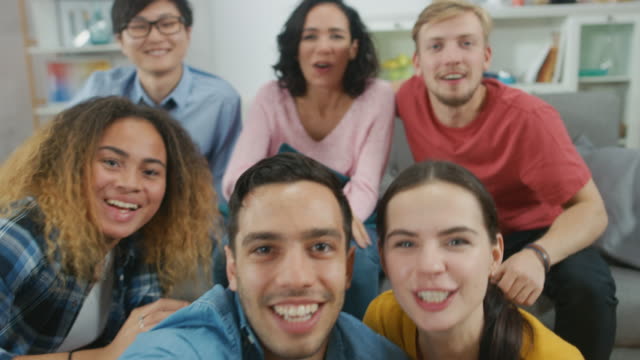 At-Home-Diverse-Group-of-Friends-Doing-Collective-Video-Stream,-Guy-Holds-Camera.-People-Smile,-Laugh,-Wave-and-Greet-Viewers.Young-People-Doing-Live-Stream-of-the-Home-Party.