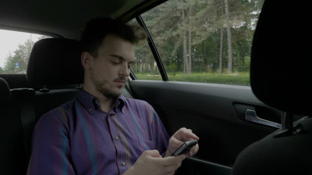 Young-entrepreneur-man-sitting-in-a-back-of-riding-uber-cab-texting-and-chatting-on-his-smartphone