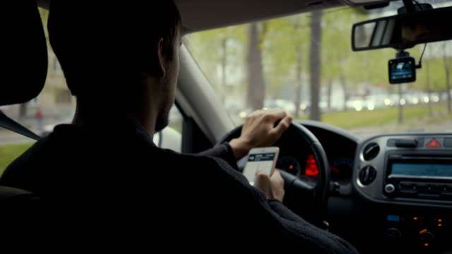 Junger-Mann-nutzt-Kartenapp-auf-seinem-Smartphone-in-einem-Auto-Fußjunge-Fahrerin-hinter-dem-Steuer.-4k