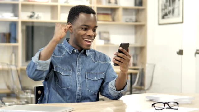 Aufgerufener-afrikanischer-Mann,-der-Erfolg-genießt,-während-er-Smartphone-benutzt
