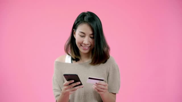 Junge-asiatische-Frau,-die-Smartphone-kauft-Online-Shopping-per-Kreditkarte-Gefühl-glücklich-lächelnd-in-lässiger-Kleidung-über-rosa-Hintergrund-Studio-Shot.-Glücklich-lächelnde-entzückende-Frau-freut-sich-über-Erfolg.
