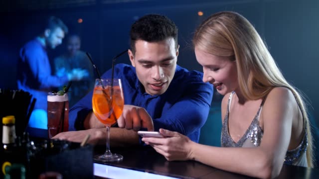 Dating-couple-using-phone-sitting-at-bar-counter