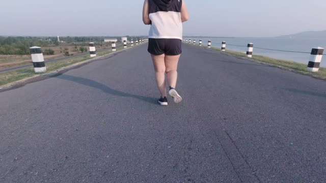 Asiatische-Frauen-joggen-in-der-Straße-am-frühen-Morgen-Sonnenlicht-am-Wasserspeicher-Pa-Sak-Jolasid-Dam.-Konzept-des-Gewichtsverlustes-mit-Bewegung-für-die-Gesundheit.-Langsame-Bewegung,-Bottom-Ansicht