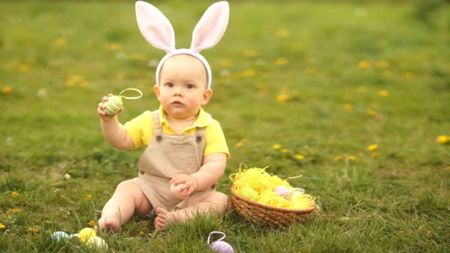 Adorable-bebé-en-un-disfraz-de-conejo-de-Pascua-recoge-los-huevos-de-Pascua-en-una-cesta-sentada-en-la-hierba-en-el-parque.-Picnic-de-primavera,-Feliz-familia-de-Pascua