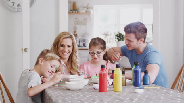 Familie-sitzt-um-Küchentisch-mit-Eltern-helfen-Kindern-Ostern-Dekorationen-zu-malen---in-Zeitlupe-gedreht