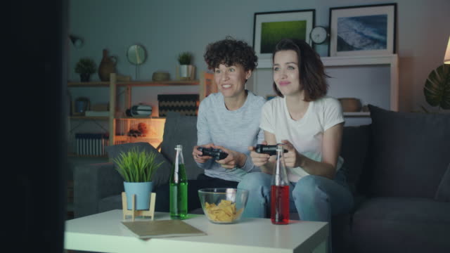 Beautiful-girls-playing-video-game-at-home-at-night-having-fun-sitting-on-sofa