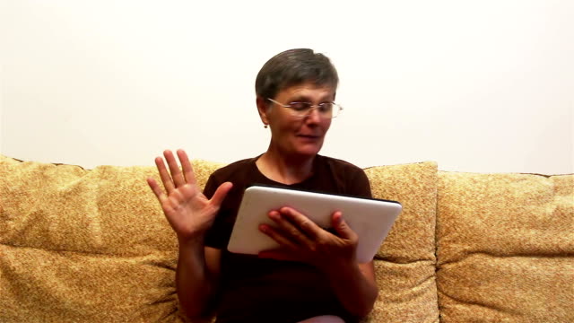 Eine-attraktive-erwachsene-Frau-ist-Video-Chat-mit-ihrer-Familie,-auf-einem-Tablet-PC,-sitzen-auf-einem-Sofa-zu-Hause.