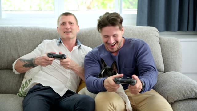 Gay-couple-relaxing-on-couch-with-dog-playing-games.-Trying-to-play-game-with-dog-on-lap.