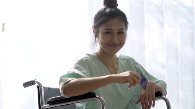 Paciente-feliz-sostener-tarjeta-de-crédito-y-sonrisa-mientras-está-sentado-en-silla-de-ruedas-en-el-hospital