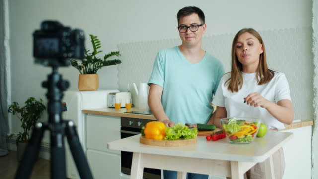 Un-par-de-bloggers-grabando-vídeo-en-la-cocina-mostrando-la-mano-agitada-con-pulgar-hacia-arriba