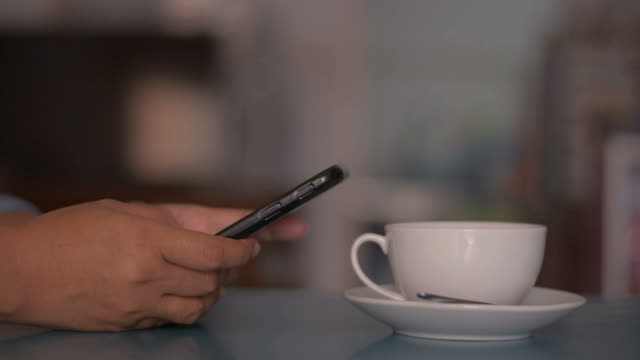 Frau-mit-Smartphone-auf-dem-Schreibtisch-und-trinken-eine-Tasse-Kaffee-zu-Hause.