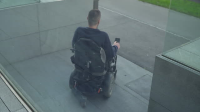 4k-Auflösung-folgen-Rückansicht-eines-Mannes-auf-elektrischen-Rollstuhl-über-eine-Rampe.-Barrierefreiheitskonzept