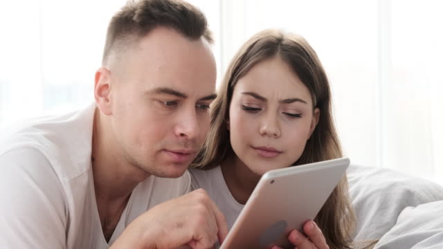 Astonished-couple-using-digital-tablet-in-bed