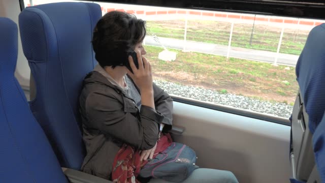 a-woman-is-sitting-on-a-train-talking-on-the-phone
