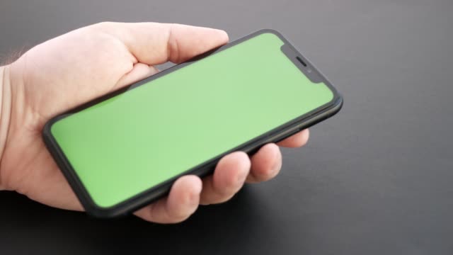 Closeup-of-a-man's-hand-holding-a-mobile-telephone-with-a-vertical-green-screen.-Man-use-smart-phone-with-touch-green-screen-for-browsing-social-networks-and-communicating-close-up