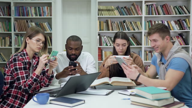 Nahansicht-ansprechender-konzentrierter-moderner-multiethnischer-Studenten,-die-ihre-Telefone-während-der-Arbeit-über-die-Universitätsaufgabe-in-der-Bibliothek-benutzen
