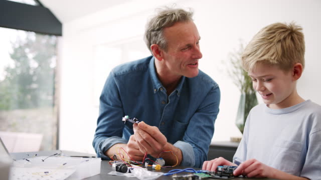 Nieto-con-abuelo-ensamblando-componentes-electrónicos-para-construir-un-robot-en-casa