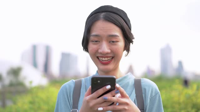Cara-de-cerca-de-la-mujer-asiática-usando-el-teléfono-inteligente.-Cara-femenina-feliz-con-dientes-blancos-cara-bonita-posando-para-retrato-de-cerca-al-aire-libre.