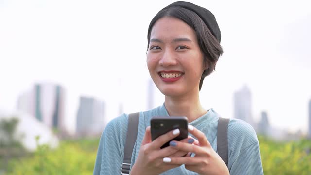 Cara-de-cerca-de-la-mujer-asiática-usando-el-teléfono-inteligente.-Cara-femenina-feliz-con-dientes-blancos-cara-bonita-posando-para-retrato-de-cerca-al-aire-libre.
