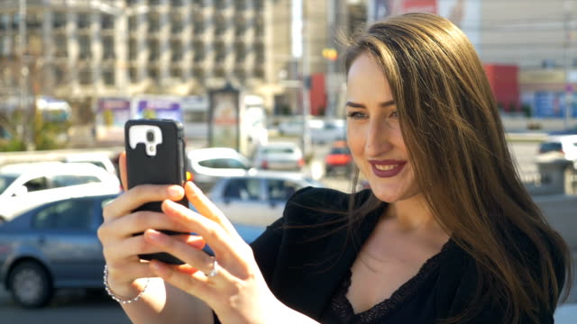Business-woman-taking-selfies-with-smartphone-camera-with-city-traffic-street-in-background
