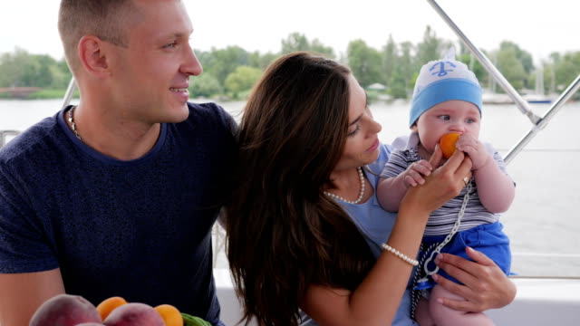parents-with-child-on-yacht,-kid-eats-first-food-on-hands-moms-on-rest,-love-couple-together-with-small-baby
