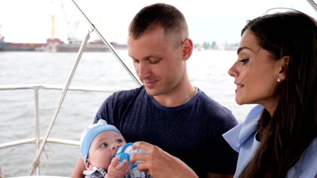 child-eating-his-first-fruits-in-hands-daddy,-family-with-baby-on-vacation,-parents-and-children-on-sea,-happy-couple-in-yacht