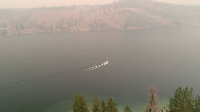 Aerial-Above-Eastern-Washington-Lake-with-Boat-Towing-Inner-Tubes-in-Wildfire-Smoke