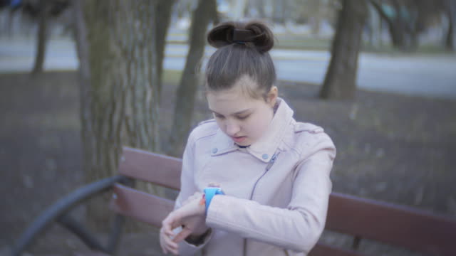 Mädchen-Teenager-sitzen-auf-einer-Bank-im-freien-und-ist-smart-Watch