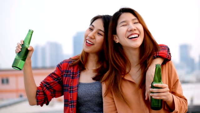Slow-motion-young-asian-woman-lesbian-couple-clinking-bottles-of-beer-party-on-rooftop.