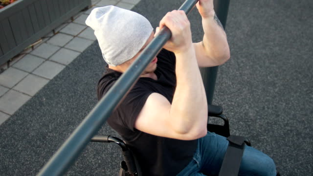 Muscular-disabled-man-in-wheelchair-pulls-up-on-the-crossbar-outdoors
