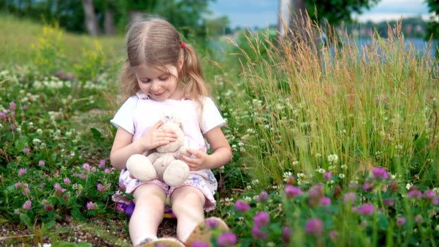 Ein-kleines-Mädchen-spielen-mit-einem-Spielzeug-Hasen-auf-der-Wiese-unter-den-blühenden-Klee