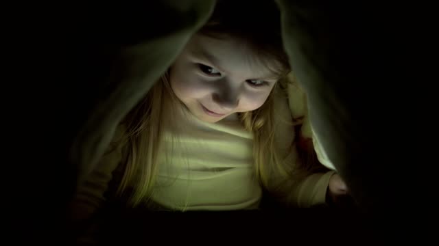 Little-girl-with-tablet-under-blanket.-Kid-at-night-with-tablet.-Girl-in-bedroom