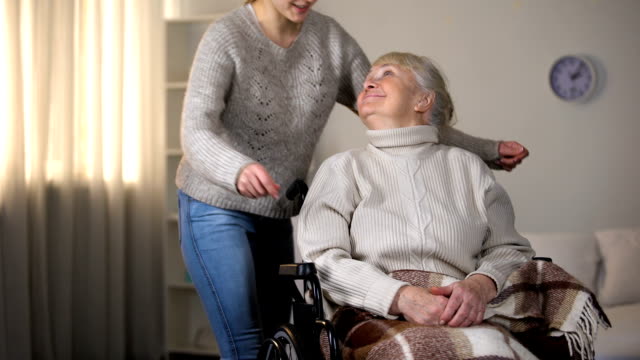 Enkelin-umarmt-lächelnd-alten-Frau-im-Rollstuhl,-familiäre-Liebe-und-Fürsorge