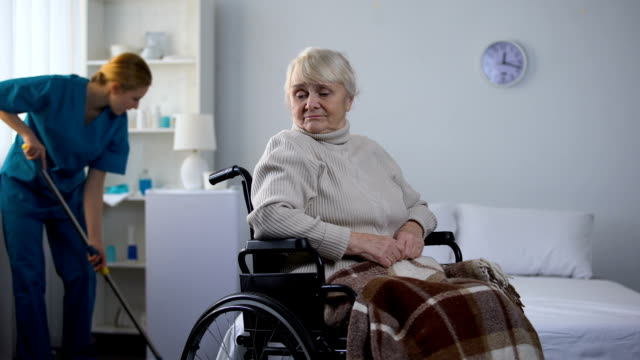 Traurige-Frau-im-Rollstuhl-gerade-Hausmeister-Reinigung-Zimmer-im-Krankenhaus,-medizinisches-Zentrum
