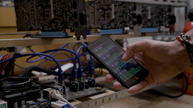 Hombre-técnico-mostrando-avances-de-software-de-minería-en-smartphone-pantalla-cerca-de-la-plataforma-de-explotación-minera-de-cryptocurrency-de-gpu