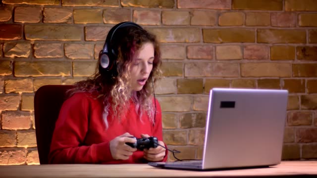 Porträt-der-jungen-Bloggerin-in-roten-Hoodie-spielen-Videospiel-mit-Joystick-und-scheiterte-mit-Blamage-auf-bricken-Wand-Hintergrund.