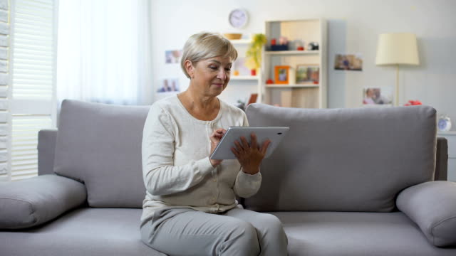 Senior-lady-shopping-online-on-tablet-at-home-smiling-at-camera,-technology