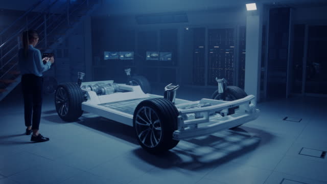 Automobile-Engineer-Working-on-Electric-Car-Chassis-Platform,-Using-Tablet-Computer-Augmented-Reality-with-3D-CAD-Software-Modelling.-Innovative-Facility:-Vehicle-Frame-with-Wheels,-Engine,-Battery