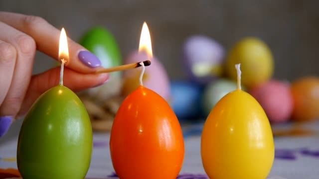 Velas-hechas-en-forma-de-huevo-de-Pascua.-Verde,-naranja,-amarillo.-La-mano-femenina-enciende-velas.