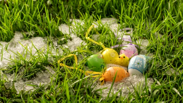 Snow-is-melting-in-green-grass-meadow-with-colorful-Easter-eggs-and-little-chick-decoration-Time-lapse