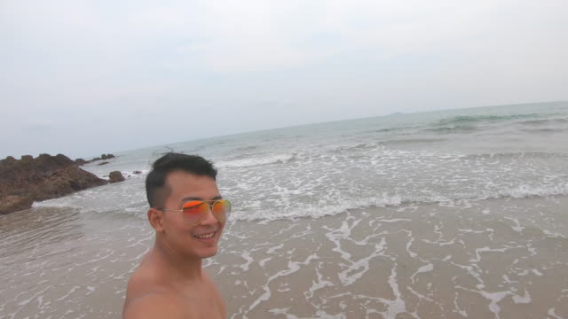 Junger-asiatischer-Mann-Taking-Selfie-Video-und-läuft-zum-Strand,-Happy-Man-Smiling-auf-Action-Camera-oder-Smartphone-und-Fotos-machen-und-Video-während-der-Urlaubsreise.-4K.