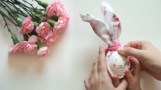Las-manos-de-las-mujeres-y-los-niños-hacen-la-decoración-de-huevo-de-pollo-para-conejo-de-Pascua-con-cara-pintada-y-orejas-de-bufanda.