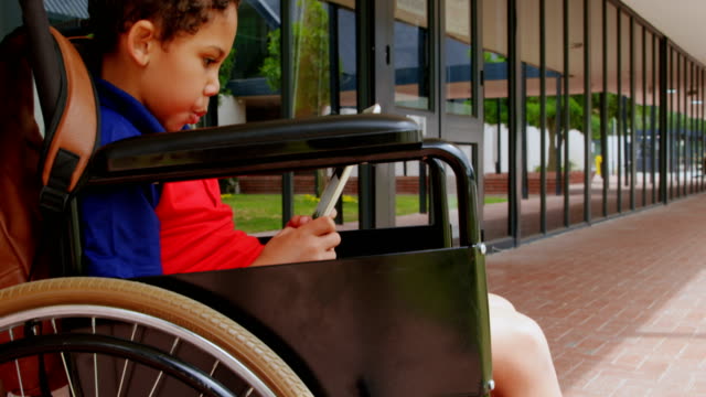 Seitenansicht-behinderter-afroamerikanischer-Schuljunge-mit-digitalem-Tablet-im-Schulkorridor-4k