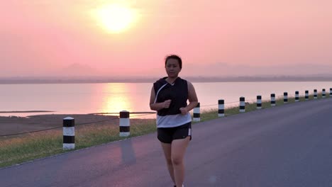 Übergewichtige-asiatische-Frauen-joggen-am-frühen-Morgen-im-Sonnenlicht-auf-der-Straße.-Konzept-des-Gewichtsverlustes-mit-Bewegung-für-die-Gesundheit.